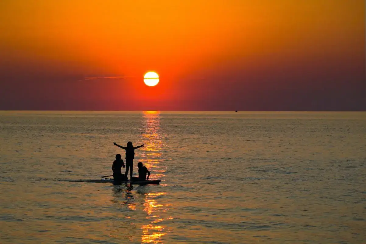 three people on a stand-up paddle board at sunset | lake erie beaches