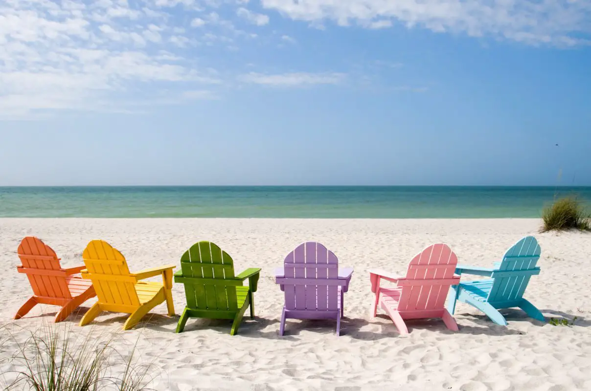 a row of brightly coloured Adirondack chairs on the beach | best beaches in ontario