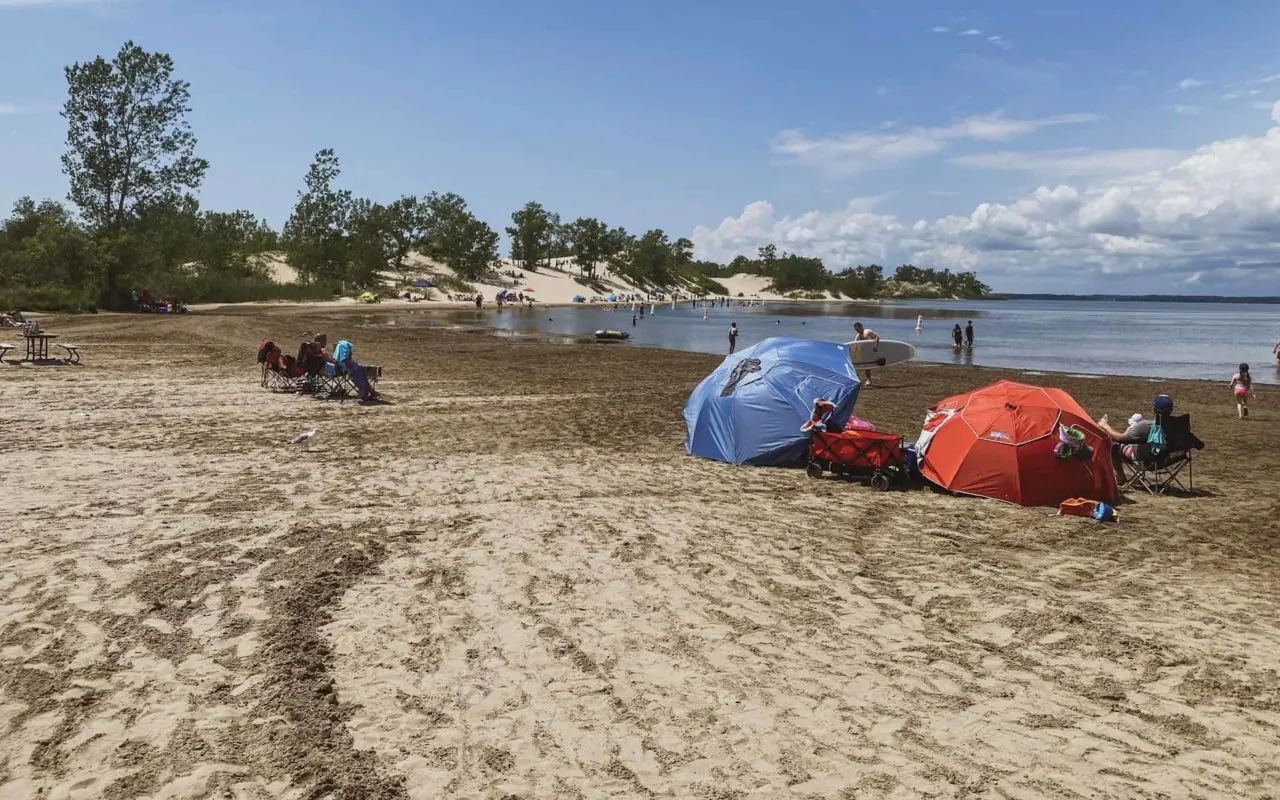 people with sun umbrellas and lawn chairs on a sandy beach | Sandbanks Beach