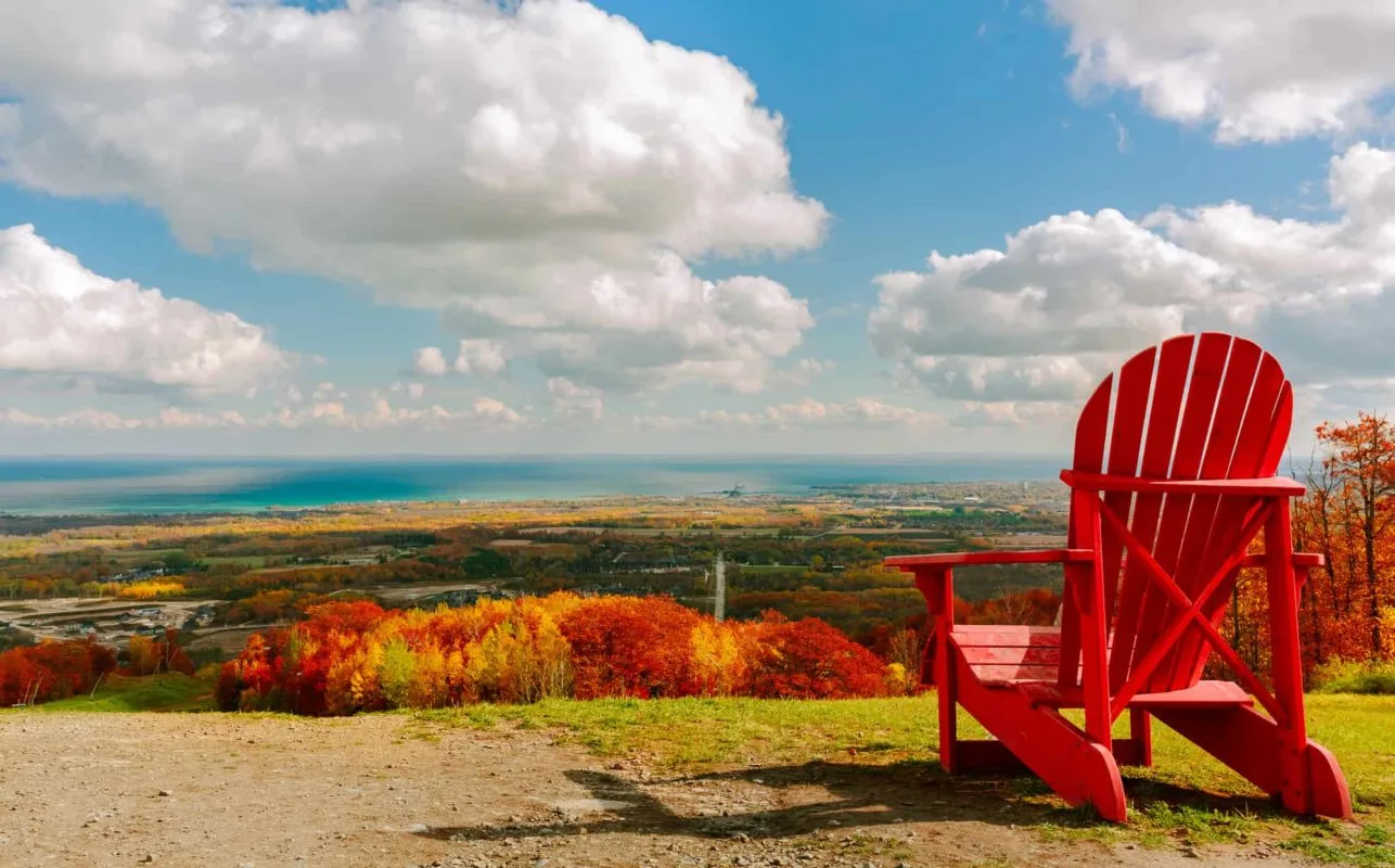 red Adirondack chair overlooking a wooded area in fall colours | places to visit in ontario in fall (1)